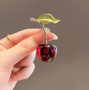 Close-up of red cherry brooch with gold leaves held in hand for scale and detail