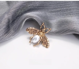 Détail de la broche abeille dorée vintage avec ailes évidées et perle goutte sur soie