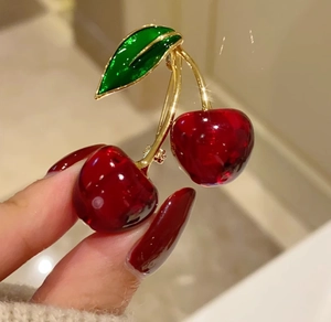 Close-up of sweet cherry brooch with deep red translucent fruit and green enamel leaves