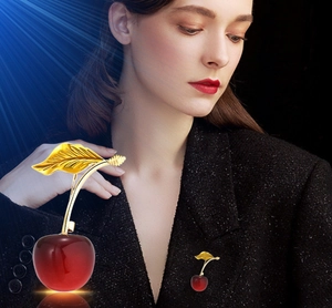 Detailed view of red cherry brooch with golden leaves on a grey suit lapel