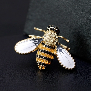 Macro shot of bee brooch with yellow rhinestones and white enamel wings on black leather
