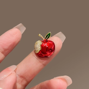 Close-up of red enamel apple brooch with gold leaf and pavé crystals held by hand
