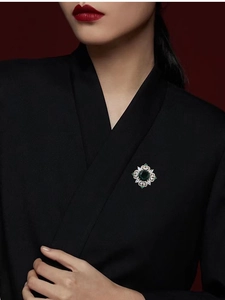 Detail view of a luxury emerald crystal brooch styled on a black garment for women