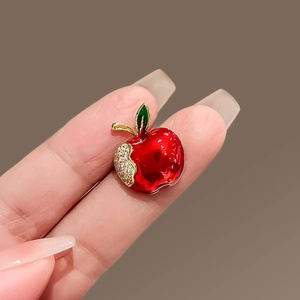 Detail of red enamel apple brooch with sparkling rhinestones held by hand for size