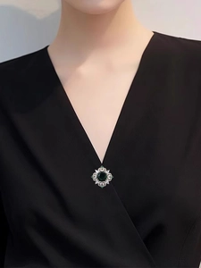Detailed view of luxury emerald crystal brooch pinned on a black V-neck dress