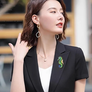 Detailed close-up of a vintage seahorse brooch with green and yellow enamel on a black lapel