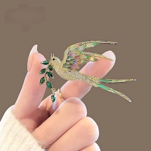 Détail d'une broche oiseau avec ailes en émail coloré et feuille en pierre verte