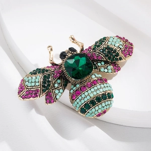 Close-up of vintage bee brooch with green crystal and colorful rhinestones on silk
