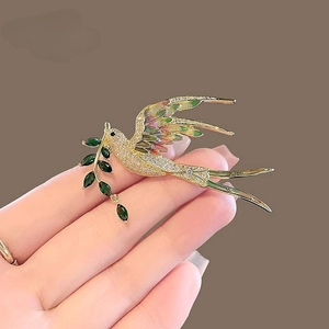 Détail d'une broche pie dorée avec ailes en émail et branche d'olivier verte sertie
