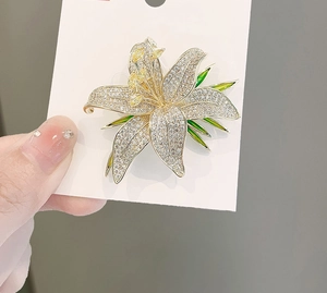 Macro view of large lily brooch featuring white crystals and green enamel leaves