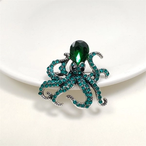 Macro shot of silver octopus brooch featuring green rhinestones and a large teardrop stone