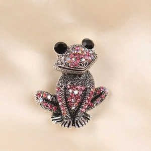 Macro detail of frog brooch featuring vintage silver metal and pink purple crystals