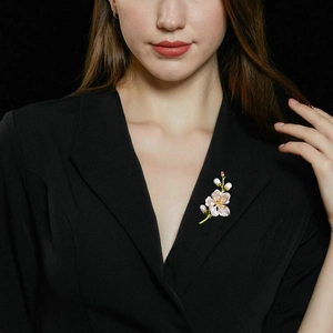 Dettaglio dell'elegante spilla a magnolia con petali rosa e perle su giacca nera da donna