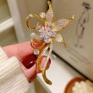 Detail of a vintage gold flower brooch with pavé crystals held by a model wearing white sweater