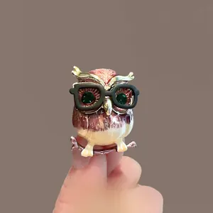 Détail macro d'une broche hibou avec finition émail dégradé et yeux en pierres vertes