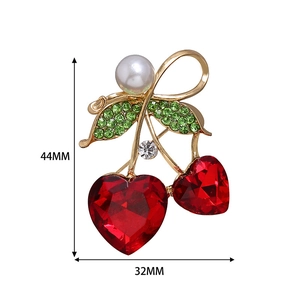 Détail macro d'une broche cerise avec cristaux cœur rouges, feuilles vertes et perle