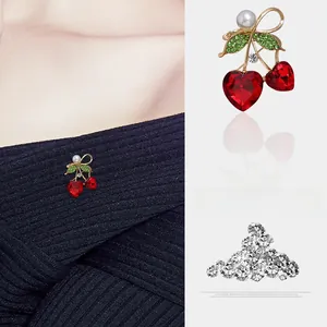Vue détaillée d'une broche cerise avec cristaux en cœur rouge et pierres vertes