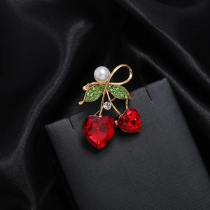 Détail d'une broche cerise avec cristaux cœur rouges, diamants verts et perle blanche
