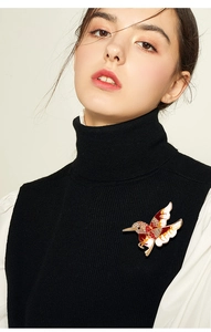 Détail de broche colibri avec strass et émail fixée sur un pull en maille noire