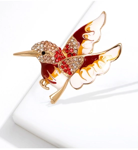 Détail macro d'une broche colibri avec émail coloré et strass brillants sur fond gris