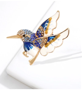 Détail macro d'une broche colibri avec strass colorés et émail bleu sur support doré