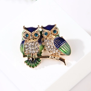 Detailed view of enamel owl brooch with vibrant blue and green wings on gold branch