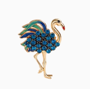 Broche flamant dorée avec cristaux bleu foncé et plumes en émail vert sur fond blanc neutre
