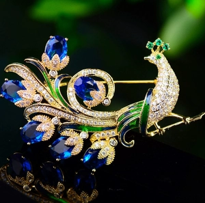 Élégante broche paon dorée sertie de cristaux bleus et verts sur surface noire réfléchissante