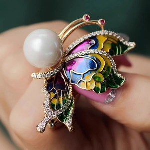 Vue macro d'une broche papillon avec ailes en émail coloré et une grande perle ronde