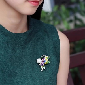 Vue détaillée d'une broche papillon en émail avec une grande perle blanche et cristaux