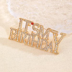 Gros plan d'une broche dorée 'IT'S MY BIRTHDAY' avec des strass étincelants et une pierre rouge