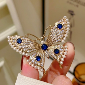 Detailed close-up of butterfly brooch with white pearls, crystals, and blue gemstones