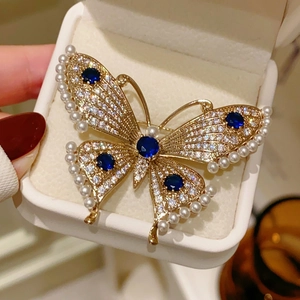Close-up of a luxury pearl butterfly brooch with blue rhinestones held in a gift box