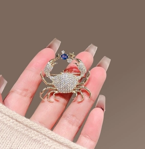 Close-up of a crab brooch featuring sparkling crystals and a central deep blue gemstone