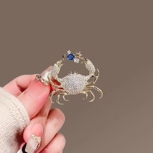 Close-up of golden crab brooch with sparkling zircons and a deep blue center gemstone