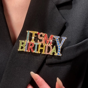 Détail de la broche colorée 'IT'S MY BIRTHDAY' en strass sur une veste de costume noire