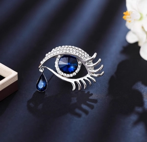 Macro shot of silver evil eye brooch with blue crystals and a drop pendant on silk