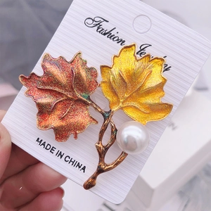 Detailed close-up of a vintage enamel maple leaf brooch with a large white pearl detail