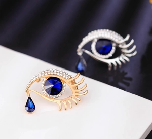 Detailed macro view of evil eye brooches with blue crystal and teardrop pendant