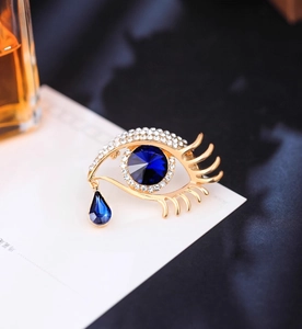 Macro shot of evil eye crystal brooch with gold plating and blue teardrop pendant