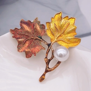 Detailed macro shot of vintage enamel maple leaf brooch with a large white pearl accent