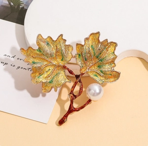 Detail of maple leaf enamel brooch with golden glitter finish and elegant pearl accent