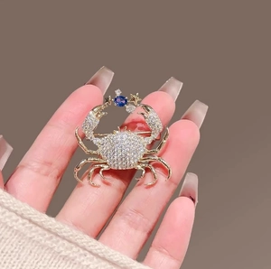 Exquisite gold crab brooch with blue gemstone and sparkling crystals held by hand