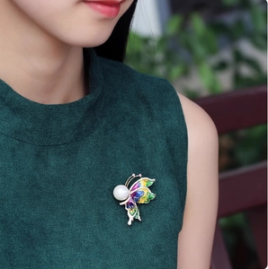 Broche papillon élégante aux ailes en émail coloré et perle sur un pull en maille verte