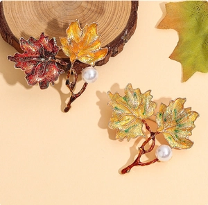 Detail view of enamel maple leaf brooches with autumn gradient colors and white pearl accents