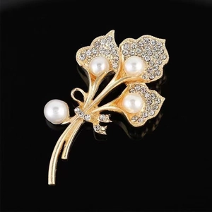 Broche bouquet dorée élégante avec perles blanches et strass brillants sur fond noir