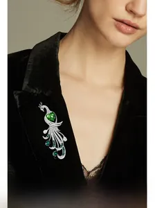Detailed shot of a luxury peacock brooch with green heart gemstone on a black velvet blazer
