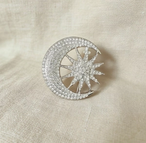 Close-up of sun and moon brooch with sparkling crystals on a textured linen fabric
