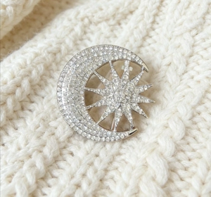 Macro shot of star and crescent moon brooch with crystals on white knit fabric