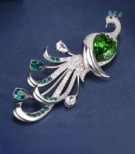 Macro detail of luxury peacock brooch with green heart gemstone and silver-tone finish